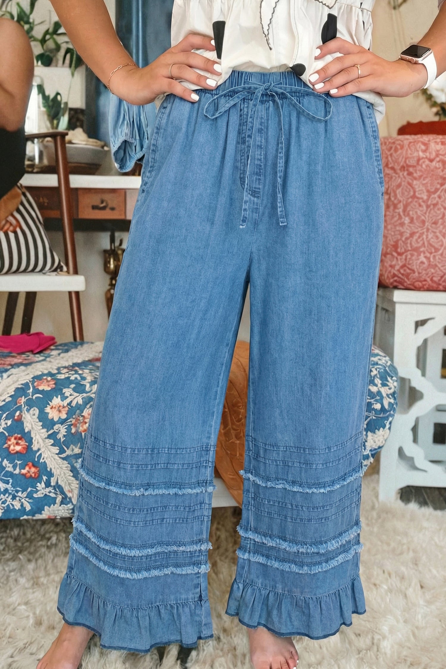 Person wearing blue denim pants with ruffled bottom hem in a casual setting.