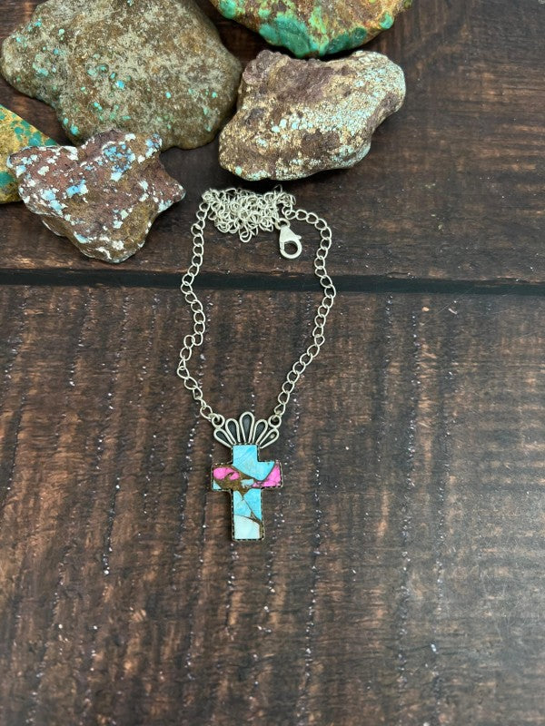 Necklace with a turquoise cross pendant on a wooden surface with rocks in the background