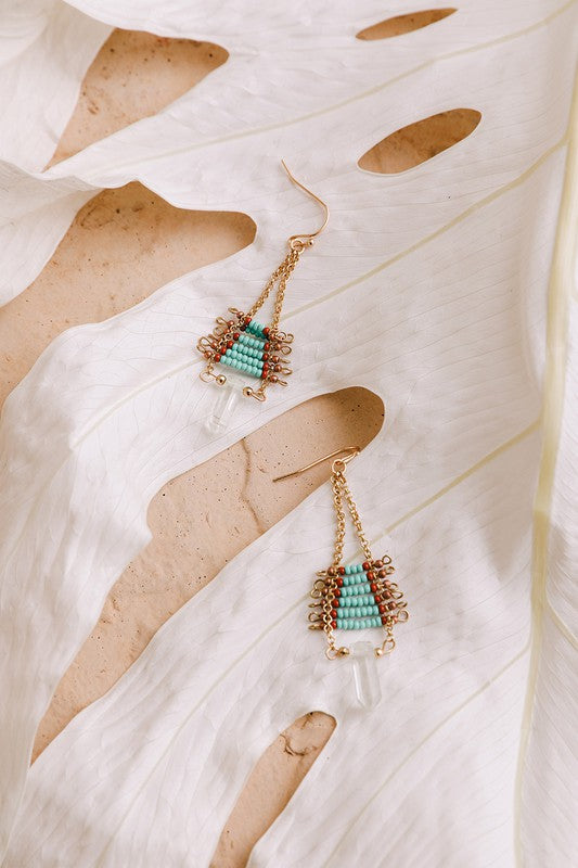 Pair of gold and turquoise beaded earrings on a textured white surface