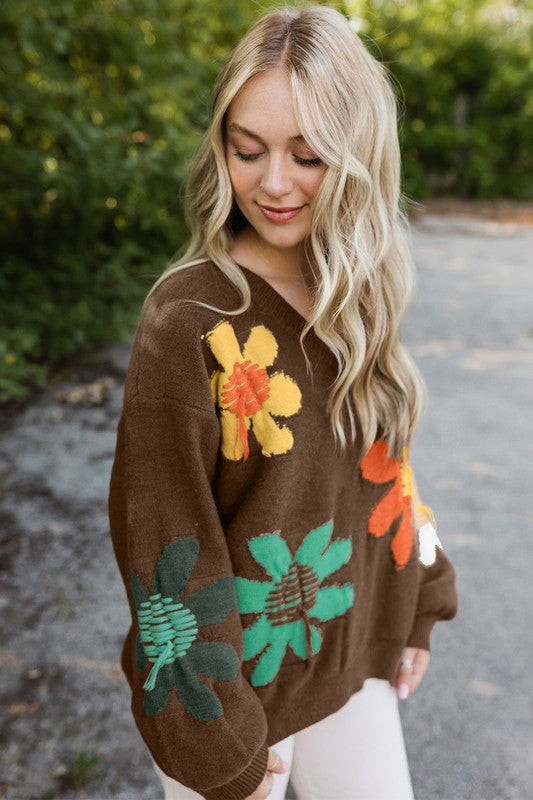 Woman wearing a brown sweater with colorful floral patterns outdoors.