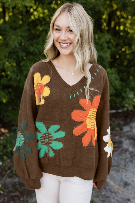 Woman wearing a brown sweater with colorful floral patterns outdoors.