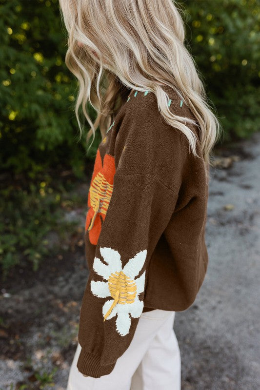 Person wearing a brown sweater with floral designs outdoors