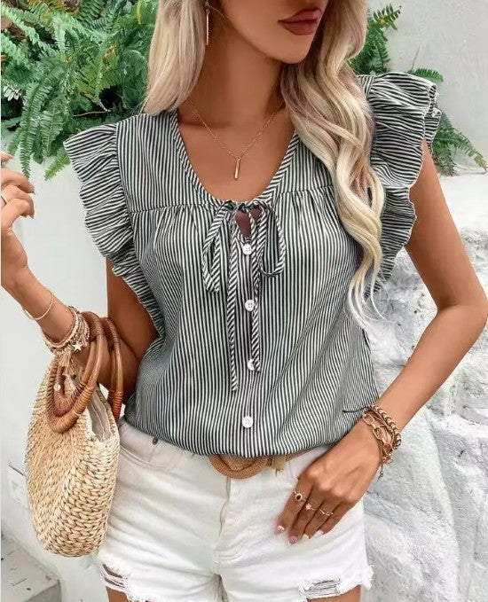 Woman wearing a striped blouse with ruffled sleeves and white shorts, holding a straw bag.